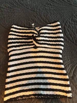 Randig stickad tubtopp svart/vit - Säljer en stickad tubtopp i svart och vitt med horisontella ränder. Toppen har en twistdetalj framtill och är axelbandslös, perfekt för en trendig och avslappnad look. Materialet är mjukt och stretchigt för skön passform. Har lappen kvar!! 