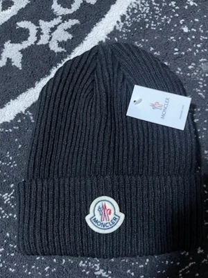 Svart ribbstickad mössa Moncler - Snygg svart ribbstickad mössa från Moncler med uppvikt kant och klassisk Moncler-logga framtill. Tillverkad i mjukt material som håller dig varm och stilen on point. Perfekt accessoar för kalla dagar.