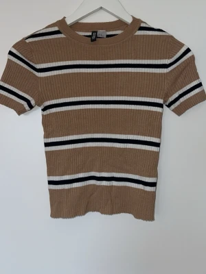 Randig ribbad topp från H&M - Snygg ribbad topp från H&M i beige med svarta och vita horisontella ränder. Kortärmad modell med rund halsringning och figurnära passform. 
