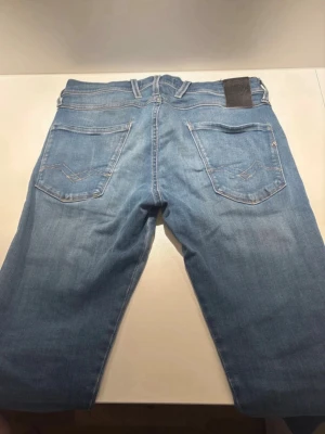 Ljusblå raka jeans med patchdetaljer - Säljer ett par ljusblå jeans med raka ben och coola patchdetaljer på baksidan av benen. Jeansen har klassiska bakfickor med dekorativa sömmar och bälteshällor. Perfekta för dig som gillar en avslappnad och trendig stil.