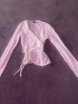 Vit spetsomlottopp från Gina Tricot - Säljer en vit omlottopp från Gina Tricot i spets med långa ärmar och knyt i midjan. Toppen har en v-ringad hals och är perfekt för dig som gillar romantiska detaljer och en feminin look.