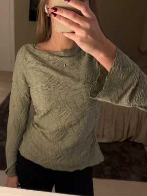 Grön ribbad långärmad topp - Trendig grön långärmad topp med ribbad struktur och vågigt mönster. Toppen har en något lös passform och är tillverkad i ett mjukt, stretchigt material som känns bekvämt mot huden. Perfekt att styla med både jeans och kjol.