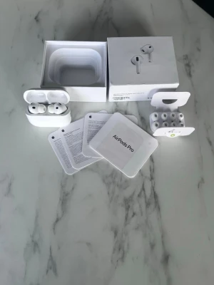 Apple AirPods Pro trådlösa hörlurar - Säljer ett par vita Apple AirPods Pro med laddningsetui, extra silikontoppar och originalförpackning. Hörlurarna är in-ear och har en stilren, minimalistisk design i blankt plastmaterial. Perfekta för dig som vill ha grymt ljud och smidig trådlös upplevelse.