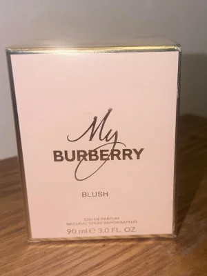 My Burberry Blush Eau de Parfum - Fräsch och feminin parfym från Burberry, My Burberry Blush, i en elegant ljusrosa kartong med gulddetaljer. Flaskan innehåller 90 ml Eau de Parfum och har en lyxig och modern design som passar perfekt på parfymhyllan.