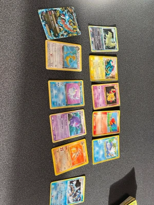 Pokémonkort samling blandade kort - En samling Pokémonkort med olika motiv och färger, inklusive både vanliga och holografiska kort. Bland korten finns vatten-, eld-, psykisk- och mörktyp Pokémon samt ett specialkort med glansig yta. Perfekt för samlare eller Pokémonfans.