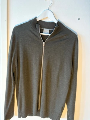 Grå ziptröja från lindbergh  - Snygg grå ziptröja från lindbergh med hög krage och asymmetrisk dragkedja. Tillverkad i mjukt, tunt material som ger en clean look. Perfekt till lager-på-lager och funkar året runt. Långärmad och minimalistisk design.