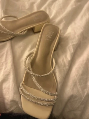 Beige klackskor med pärlband  - Säljer ett par beige pumps från Dinsko med fyrkantig tå och låg blockklack. Skorna har tre tunna remmar framtill dekorerade med små pärlor som ger en elegant touch. Perfekta för dig som gillar stilrena och trendiga skor. De är använda endast en gång.