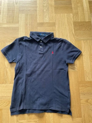 Mörkblå pikétröja från Polo Ralph Lauren - Säljer en riktigt snygg polo Ralph lauren piké, det finns inga defekter på pikén och den är i barn storlek xl som ungefär  motsvarar S i vuxen storlek. Nypris på pikén ligger på ca 1000kr men jag säljer den för endast 450kr Har endast använts en sommar.