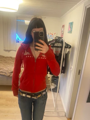 Röd zip-hoodie från Abercrombie - Säljer en röd hoodie från Abercrombie & Fitch med vit text på bröstet. Hoodien har dragkedja, två fickor fram och en huva. Luvan har ett snyggt stickat mösnster inuti😻Är medium men passar bra på mig som har S💞💞