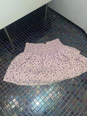 Ljuslila blommig volangkjol - Supersöt kort kjol med volanger i ljuslila och vitt blommönster. Perfekt att ha till sommaren. TAR GÄRNA EMOT PRISFÖRSLAG💗