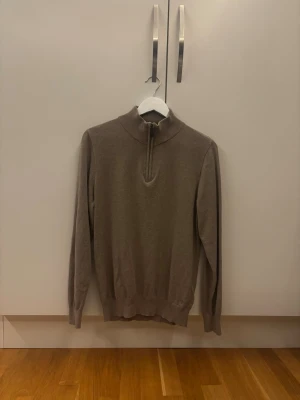 Beige stickad tröja med halvzip - Snygg beige stickad tröja med halvzip och hög krage. Tröjan har långa ärmar och ribbade muddar vid ärmslut och nederkant. Perfekt för lager på lager och enkel att matcha med olika outfits. Är i Storlek M men passar utmärkt i storlek S.