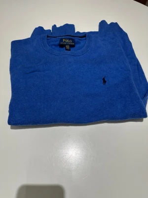 Polo Ralph Lauren tröja - Snygg blå stickad tröja från Polo Ralph Lauren med rund halsringning och diskret broderad logga på bröstet. Tröjan har långa ärmar och ribbade muddar vid ärmslut och nederkant. Perfekt till jeans eller chinos. Modellen är 187 och väger 70kg och den sitter lite litet på mig. Vid frågor är det bara att skriva!