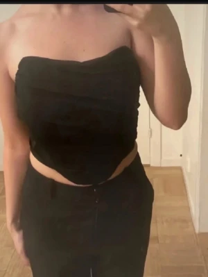 Svart bandeau tubtopp - Säljer en svart bandeau tubtopp med en snygg, enkel design. Toppen är axelbandslös och har en croppad passform som ger en trendig look. Perfekt att matcha med höga byxor eller kjol.