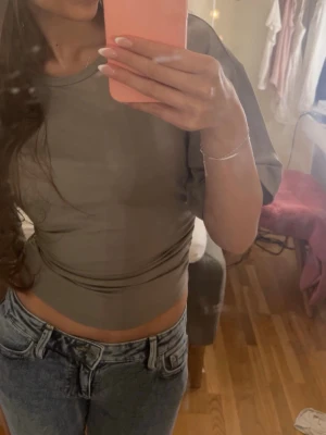 Beige croppad topp från Gina Tricot - Säljer en beige topp från Gina Tricot. Toppen har korta ärmar och en tight passform runt midjan medan den är större över armarna och bröstet. Perfekt att matcha med jeans eller kjol för en trendig look.