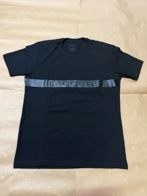 Svart Lacoste Till -shirt - Helt ny har aldrig använts. Storlek S