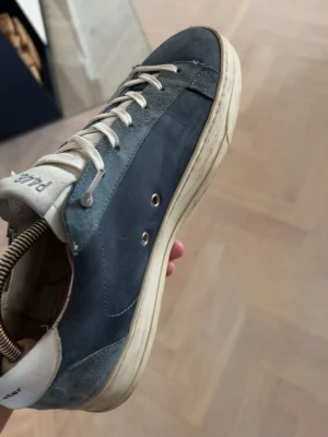 Mörkblå sneakers från P448 - Snygga mörkblå sneakers i mocka och läder. Skorna har vita detaljer, perforerade sidor och vita snören. Klassisk låg modell med vit sula och diskret logga på hälen. Perfekta för en stilren och avslappnad look.