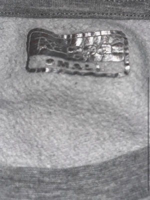 Grå sweatshirt från Kappa - Säljer en grå sweatshirt från Kappa med det klassiska svarta logotrycket framtill. Tröjan är i mjukt material och har rund halsringning. Perfekt för en avslappnad och sportig stil. Passar dig som gillar streetwear och enkel design.