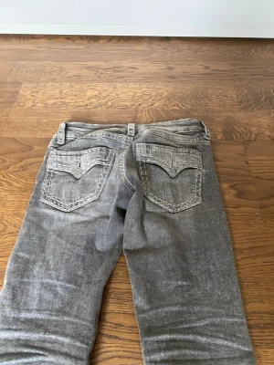 Grå bootcut jeans med fickor - Säljer ett par grå bootcut jeans med snygga bakfickor och klassisk femficksmodell. Jeansen har en lätt tvättad look och är tillverkade i denim med stretch. Perfekta för dig som gillar en avslappnad men trendig stil.
