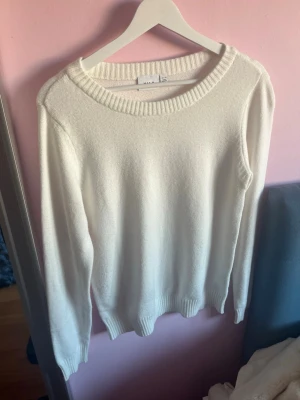 Vit stickad tröja från vila - Klassisk vit stickad tröja från vila med rund halsringning och ribbade muddar vid ärmslut och nederkant. Tröjan har en enkel och stilren design, perfekt att matcha med olika outfits. Materialet ser mjukt och bekvämt ut.