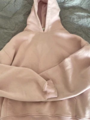 Ljusrosa hoodie med huva - En enkel och stilren ljusrosa hoodie med huva och ribbade muddar. Hoodien har en klassisk passform och är tillverkad i mjukt bomullsmaterial. Perfekt för en avslappnad och bekväm look. Har några fläckar som jag ej vet om de går bort i tvätten.