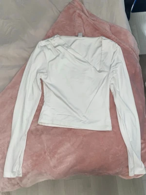 Vit asymmetrisk långärmad topp - Säljer en vit långärmad topp från H&M med asymmetrisk halsringning och figurnära passform. Toppen är tillverkad i ett mjukt och stretchigt material som känns skönt mot huden. Perfekt för basic outfit till sommaren! 🩷Tröjan är i storlek M men är ganska liten till storleken så passar lika bra till dig som har XS eller S! 