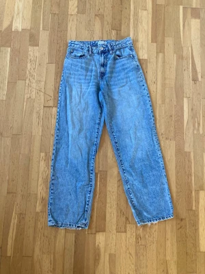 Gråblå raka jeans från ginatricot  - Säljer ett par klassiska gråblå jeans från ginatricot med raka ben och femficksmodell. Jeansen har en snygg tvättad look och läderpatch bak i midjan. Perfekta för dig som gillar en enkel och tidlös stil.