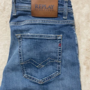 Blå raka jeans från Replay - Snygga blå jeans från Replay med klassisk femficksmodell och raka ben. Jeansen har en tydlig logotyp på bakfickan och läderpatch i midjan. Tillverkade i slitstark denim med en lätt tvättad look och kontrastsömmar. Skickar samma dag vid köp🤩
