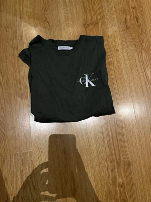 Svart Calvin Klein t-shirt - Snygg svart t-shirt från Calvin Klein Jeans med klassisk CK-logga tryckt på bröstet. T-shirten har rund hals och korta ärmar, tillverkad i mjuk bomull för skön känsla. Perfekt till jeans eller shorts för en clean look.
