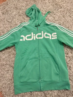 Grön adidas zip up - Super snygg adidas kofta! Den är mörkare i verkligheten men ser ljusare ut på bild pga ljuset, den är sönder i ena snöret men det är inget man tänker på❣️ det är storlek S