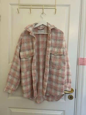 Rutig overshirt från stradivarius  - Säljer en oversized rutig overshirt från stradivarius i rosa och vitt med svarta detaljer. Skjortjackan har stora bröstfickor med knappar, klassisk krage och grov textur. Perfekt att slänga över en hoodie eller t-shirt för en chill look.