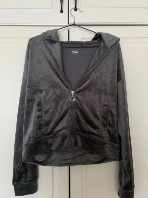 Grå velour hoodie från FILA - Mjuk och snygg grå hoodie från FILA i velourmaterial. Dragkedja framtill med FILA-logga på zipparen, två fickor och huva. Perfekt för en chill och sportig look. Oversized känsla och riktigt skön att ha på sig.💕