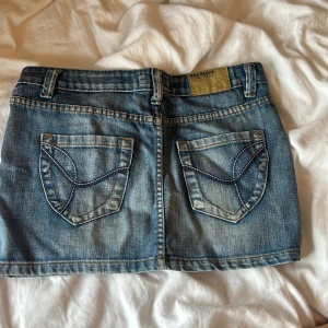 Jeanskjol från Vida Denim - Säljer en snygg jeanskjol från Vida Denim. Den är i klassisk blå denim med en dragkedja och knapp framtill. Kjolen har två bakfickor med coola sömmar och en bekväm passform. Perfekt för en avslappnad sommarlook! Dragkedjan är sönder därav priset, men går säkert att fixa!