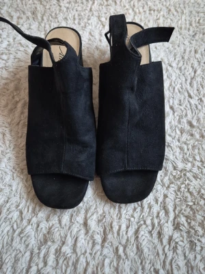 Svarta sandaler från Alley - Säljer ett par svarta sandaler från Alley i storlek 37. De har öppen tå, bred ovandel och justerbar rem runt hälen. Materialet är mockaliknande och sulan är ljus. Perfekta för dig som gillar stilrena och bekväma skor.