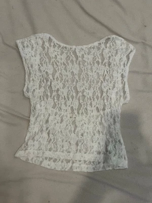 Vit spets topp med öppen rygg - Snygg vit topp i spets med blommigt mönster och öppen rygg. perfekt som fest tröja eller bara en varm sommar dag. Passar till både jeans och kjol för en fin outfit.