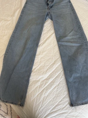 Ljusblå raka jeans - Säljer ett par ljusblå jeans med rak passform och klassisk femficksdesign. Jeansen har hög midja och är tillverkade i ett slitstarkt denimtyg. Perfekta för en avslappnad och trendig look.