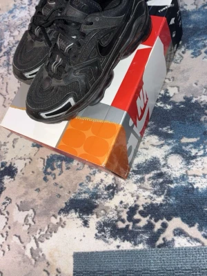 Svarta Nike Air Max Plus sneakers - Säljer ett par svarta Nike Air Max Plus sneakers med reflekterande detaljer och synlig Air-sula. Skorna har en sportig design med mesh och syntetmaterial, samt svarta snören och diskreta loggor på sidan och tungan.