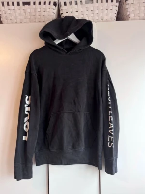 Svart hoodie från Levi's med tryck - Hoodie från Levi's. Mörk gråmelerad, "tvättad sliten look".  Med tryck på ärmarna. Storlek S. Inget ytludd. Använd men i fint skick. 
