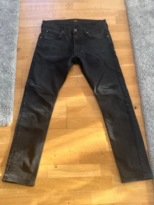 Svarta Lee slim fit jeans - Säljer ett par svarta jeans från Lee med klassisk femficksmodell och rak passform. Jeansen har metallknapp med Lee-logga och bälteshällor. Materialet är kraftig denim i bomull. Perfekta för en stilren och fräsch look. Priset är ej hugget i sten !                                                      Storlek: W30 L32