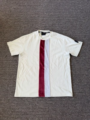 T-shirt - Säljer en vit t-shirt från la Vichy med en bred röd och en smal vit vertikal rand framtill. Klassisk rund hals och korta ärmar. T-shirten har en patch på vänster ärm och är gjord i mjuk bomull.