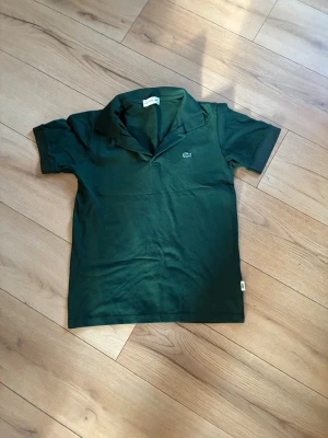 Grön piké från Lacoste - Snygg mörkgrön pikétröja från Lacoste med klassisk krage och korta ärmar. Tröjan är i storlek M men passar S även. Den går att knäppa också🫰 
