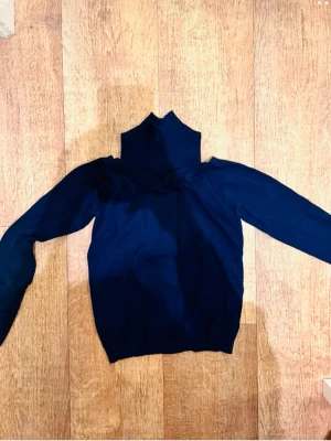 Mörkblå polotröja stickad - Mörkblå stickad polotröja med lång ärm och hög krage. Tröjan har en smal passform och ribbstickade detaljer vid kragen. Perfekt för lager på lager och enkel att matcha med olika stilar.