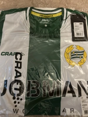 Hammarby matchtröja Craft grön/vit - Säljer en officiell äkta Hammarby IF matchtröja från Craft i grönt och vitt med klubbmärke på bröstet och JOBMAN Workwear som sponsortryck. Tröjan har klassiska breda ränder och är tillverkad i ett lätt, funktionellt material perfekt för fotboll eller träning.