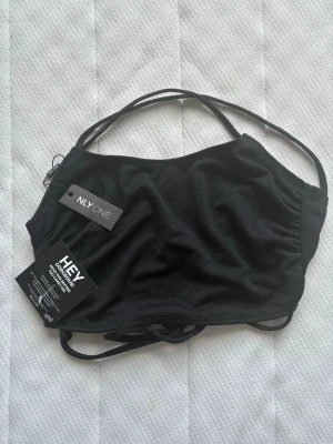 Svart croppad topp från NLY One - Stilren svart croppad topp från NLY One med tunna axelband och trendig snörning i sidan. Tillverkad i mjuk polyester som ger en skön känsla och sitter snyggt på kroppen. Perfekt att matcha med höga jeans eller kjol.