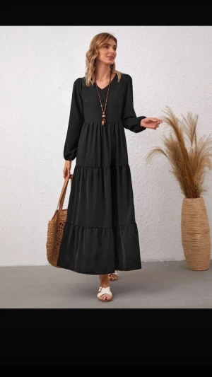 Svart Shein Klänning - Svart lång klänning med volanger för en luftig passform. Klänningen har en lätt glansig yta och stängs med dragkedja i ryggen. Passar väldigt fint som en vardagsklänning eller kan kompletteras med en tjocktröja. En liten defekt orsakad av strykjärn på framsidan har gjort att det finns ett glansigt streck, men det syns knappt!