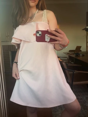 Rosa Bandoue klänning - Så fin rosa sommarklänning. Går att bära bandoue eller på en axel. Har en liten reva som inte syns när man bär klänningen (se bild 5). Står storlek 38 men jag har 34, passar även en 36. 