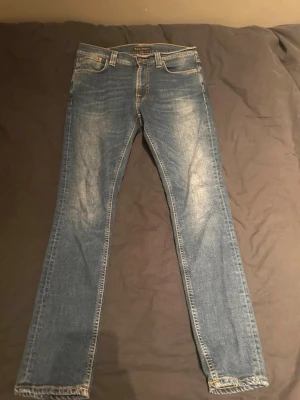 Nudie Jeans Lean Dean - Snygga blå slim fit jeans från Nudie Jeans med klassisk femficksdesign och ljusa slitningar framtill och baktill. Jeansen har raka ben och ikonisk broderad detalj på bakfickorna. Perfekta för en avslappnad och trendig look.