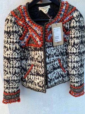 Mönstrad jacka från Isabel Marant x H&M - Unik jacka från Isabel Marant x H&M med svartvitt batikmönster och färgglada broderier i rött, blått och silver. Jackan har dragkedja framtill, rundad hals och dekorativa pärlor och paljetter på axlar och ärmslut. Perfekt statement-plagg för dig som vill sticka ut.