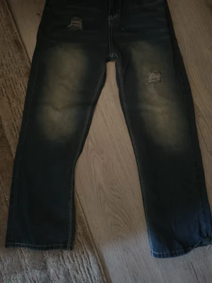 Svarta jeans med slitningar True Religion - Säljer ett par svarta jeans från True Religion med slitningar på låren och snygga kontrastsömmar. Jeansen har stora bakfickor med den klassiska hästsko-detaljen och en relaxed fit. Materialet är denim med tvättad look.