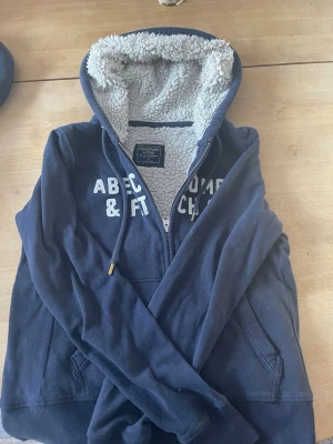 Marinblå hoodie från Abercrombie - Mysig marinblå hoodie med dragkedja från Abercrombie & Fitch. Perfekt för kalla dagar och chill vibes.  Tröjan är en s men sitter mer som en xs, passar dig dom kanske är 160-170  men skulle inte va säker om du är i den längre delen. Kan acceptera lägre bud om snabb