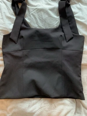 Svart topp med knytband - Svart topp från Zara med rosetter över axelbanden. Använd en gång 